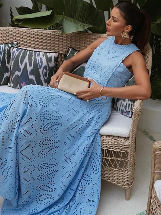 Woman in a blue lace dress sitting on a wicker chair outdoors.