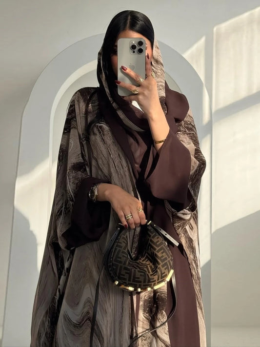Person wearing a brown outfit with a matching headscarf, holding a phone and a handbag.