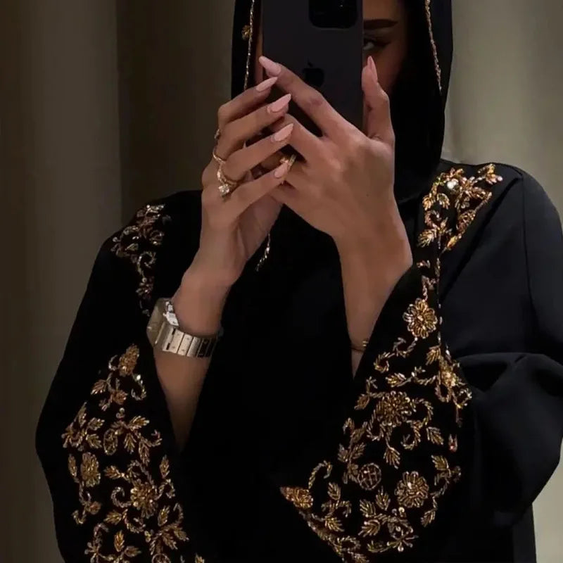 Person wearing a black embroidered garment taking a mirror selfie.