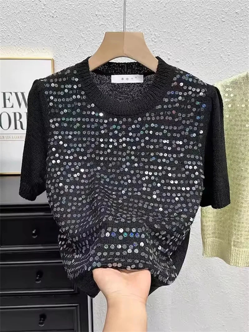 Black sequin top on a hanger against a neutral background