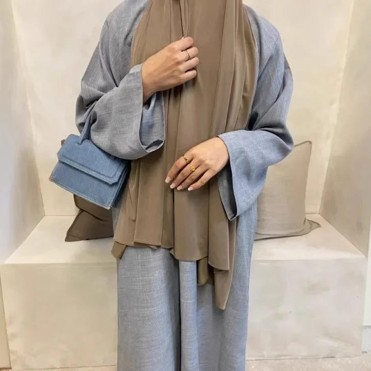 Person wearing a beige hijab and gray outfit sitting on a white bench.