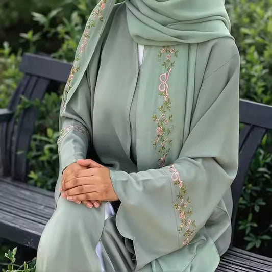 Person wearing a light green embroidered abaya sitting on a bench.