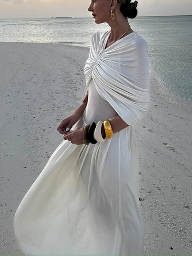 Woman in a white dress standing on a beach with 'ZAHM' branding.
