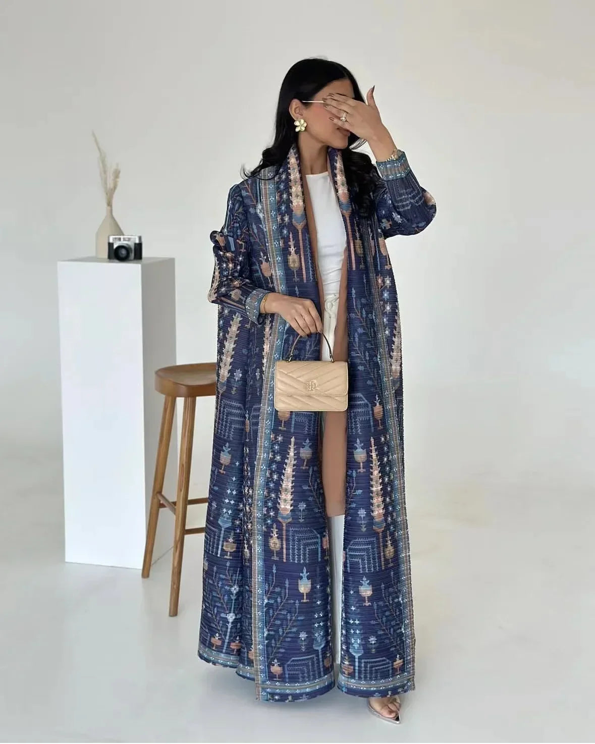 Woman wearing a long, patterned blue coat in a minimalistic setting.