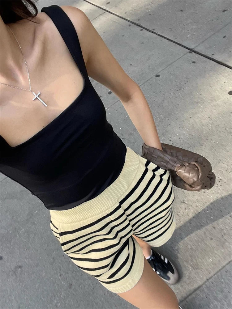 Person wearing a black top and striped shorts on a sidewalk.