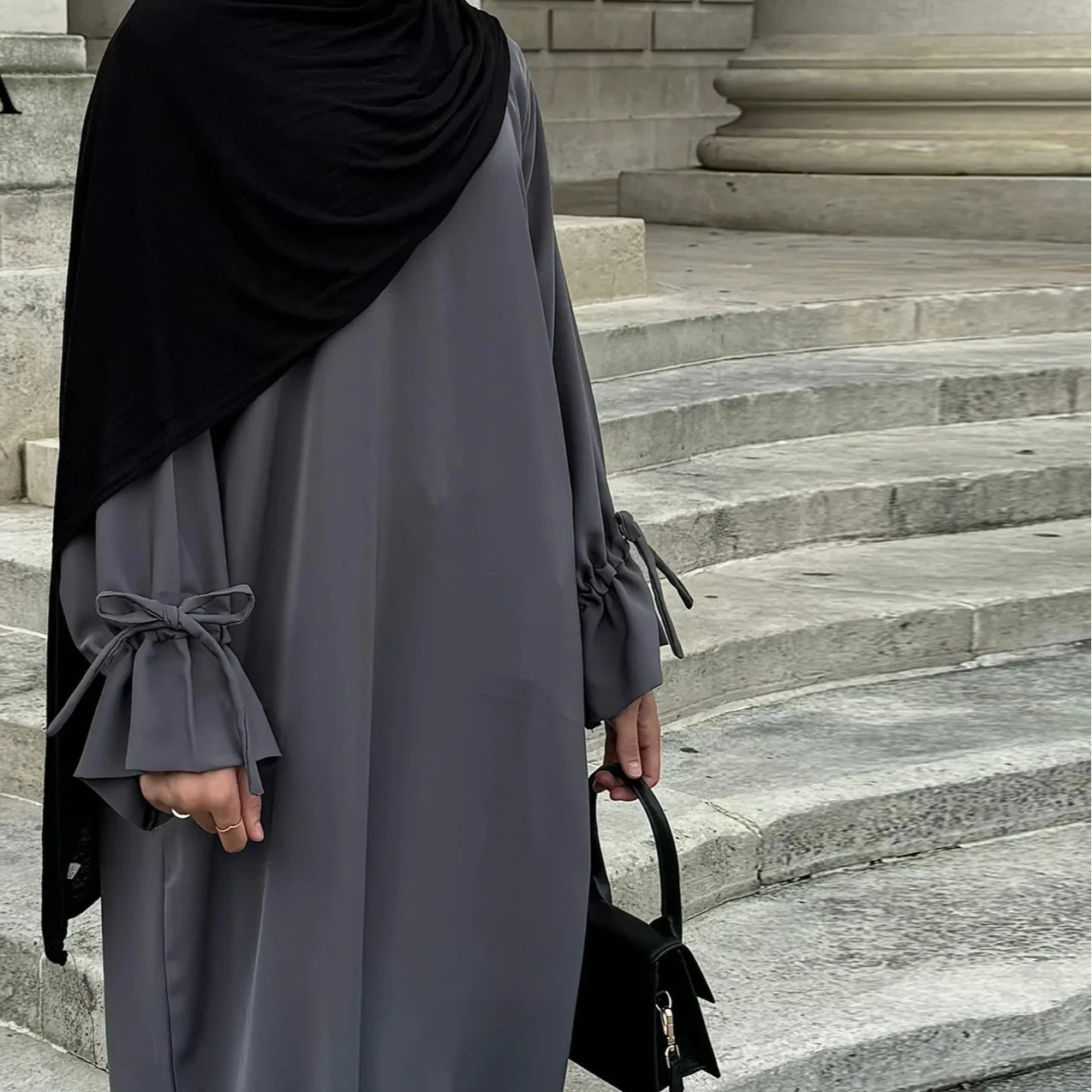 Person wearing a gray abaya with black hijab on stone steps, brand 'CPENGA' visible.