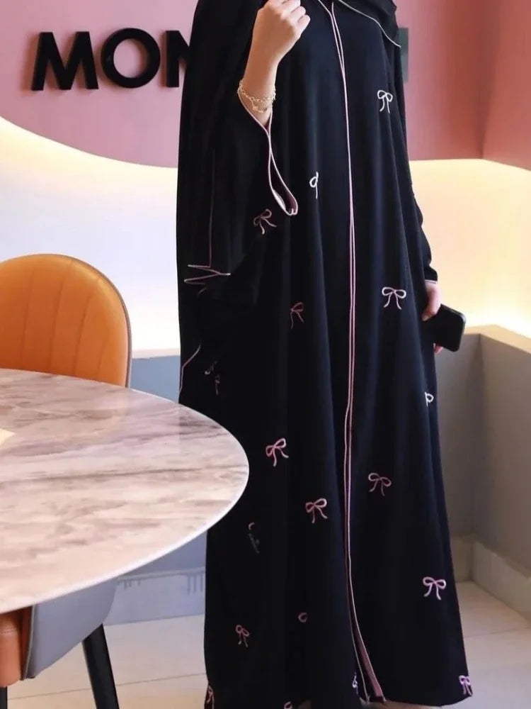Person wearing a black dress with pink bow patterns in an indoor setting.