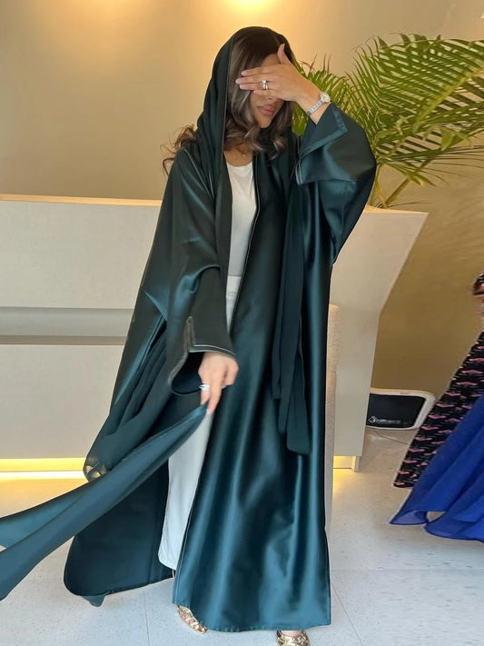 Woman wearing a long dark green robe in an indoor setting with a plant in the background.