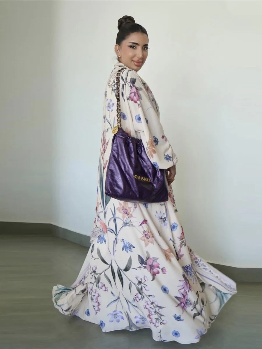Woman in a floral dress holding a purple handbag against a plain background