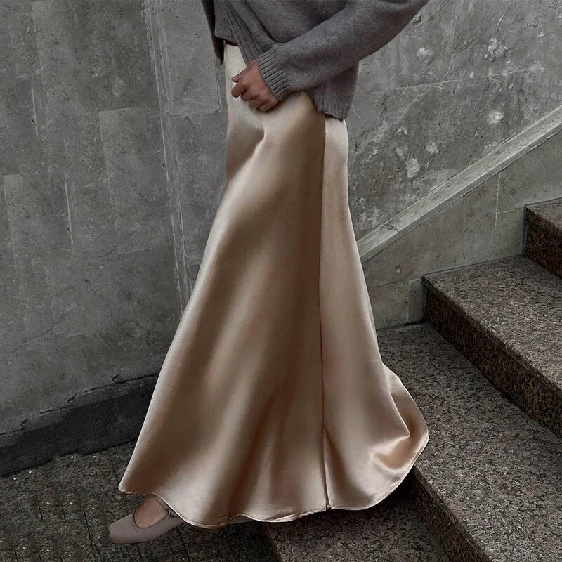 Person wearing a long beige satin skirt and gray sweater on stone steps.