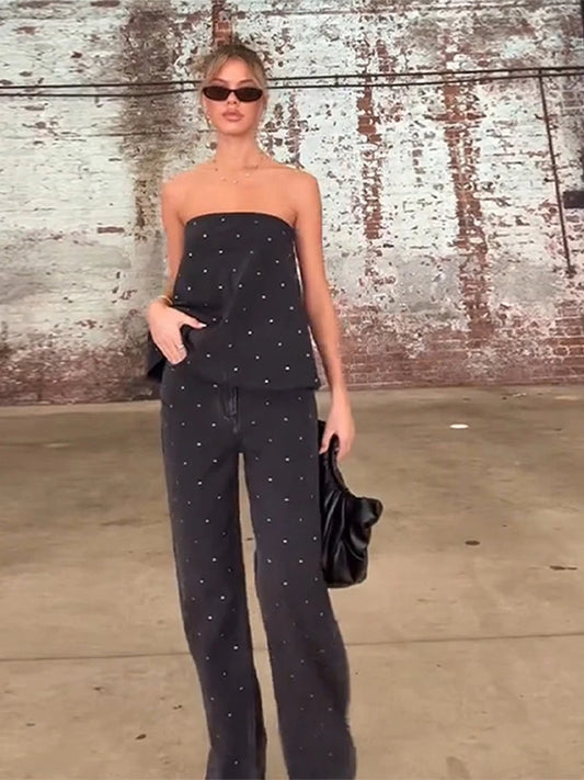 Woman in black strapless top and pants standing against a textured wall.