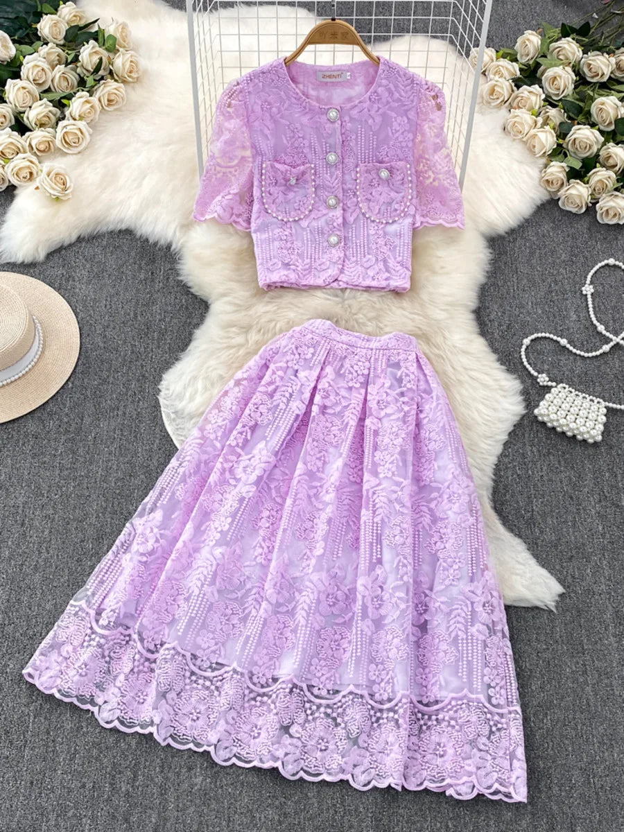 Purple lace outfit with matching top and skirt on a textured surface with flowers and a handbag.