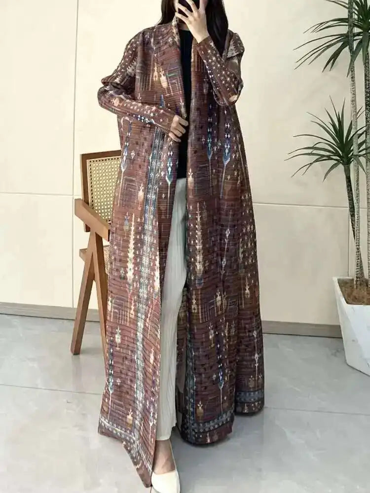 Person wearing a long, patterned coat in an indoor setting with a plant and chair in the background.