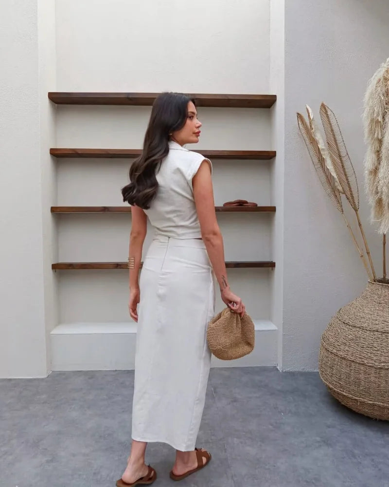 Woman in a white dress standing in a room with wooden shelves and decorative elements.