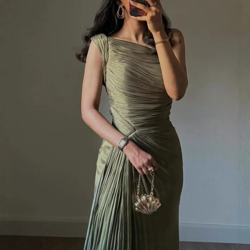 Woman in a green one-shoulder dress holding a handbag against a plain background