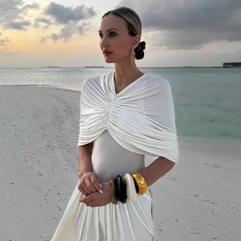 Woman in a white dress standing on a beach with a sunset in the background