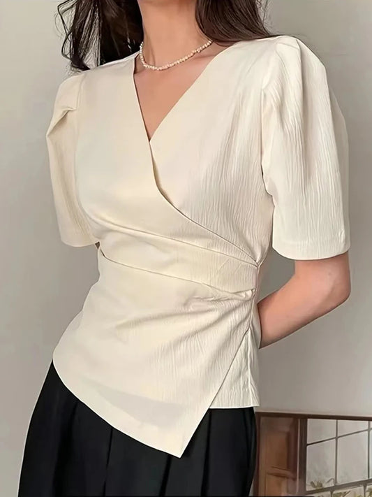 Woman wearing a cream-colored blouse with a V-neck and short sleeves against a neutral background