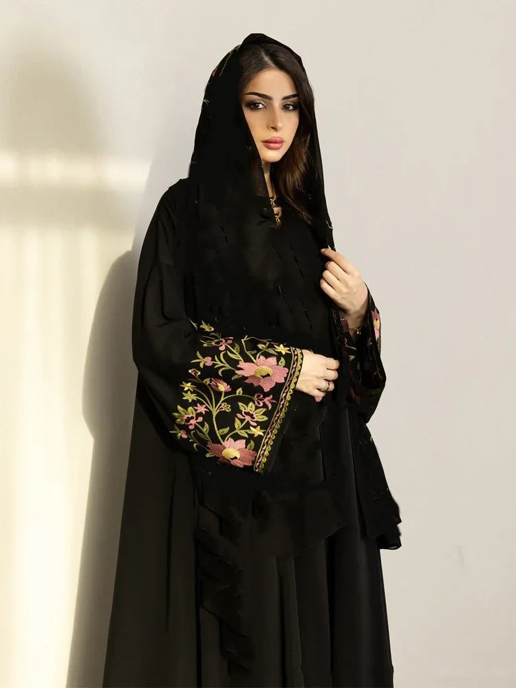 Woman wearing a black abaya with floral embroidery on a plain background