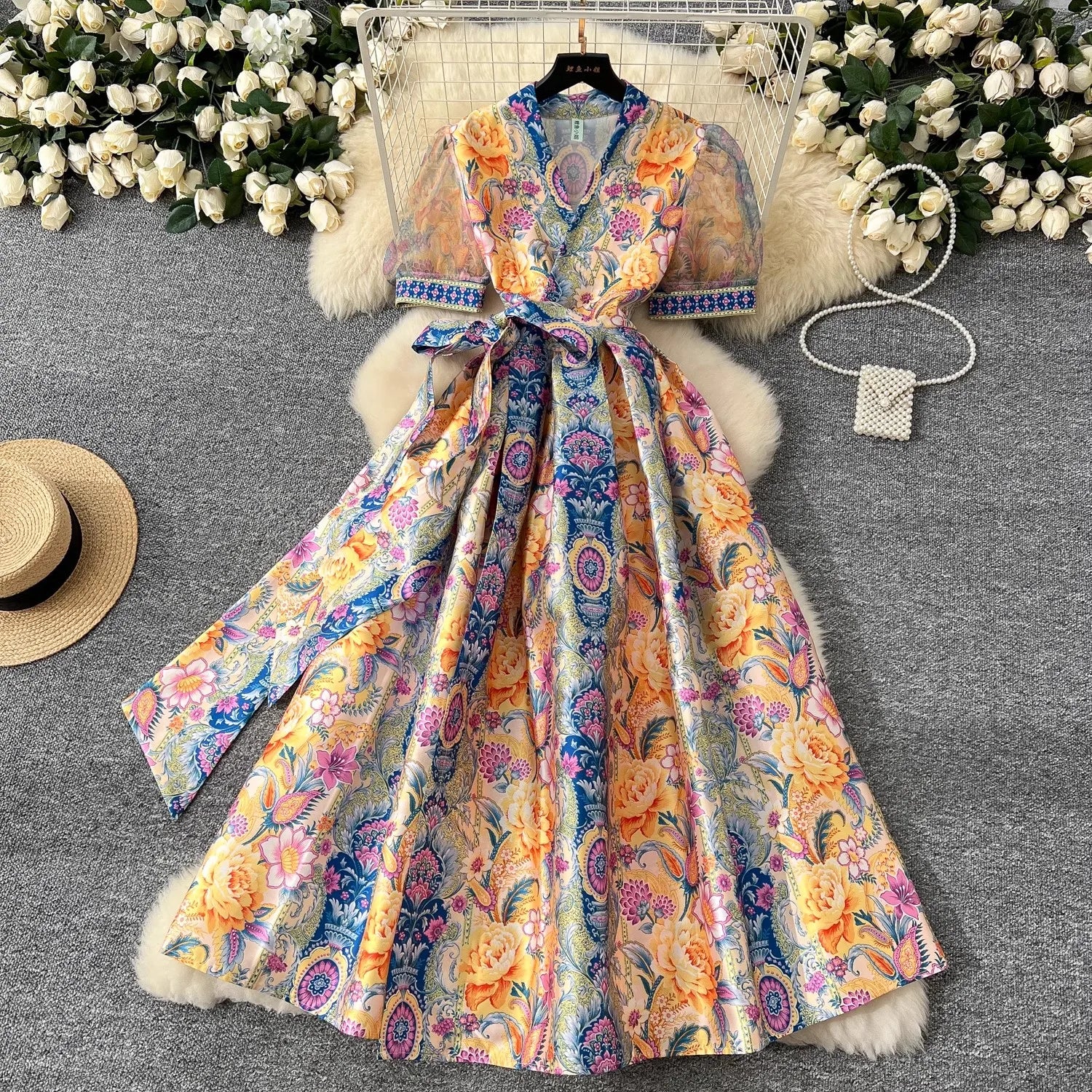 Colorful floral-patterned dress with fur trim on a textured surface with flowers in the background