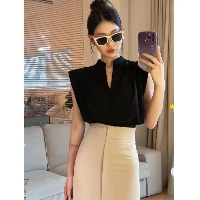 Woman taking a mirror selfie wearing a black top and beige pants in a room.