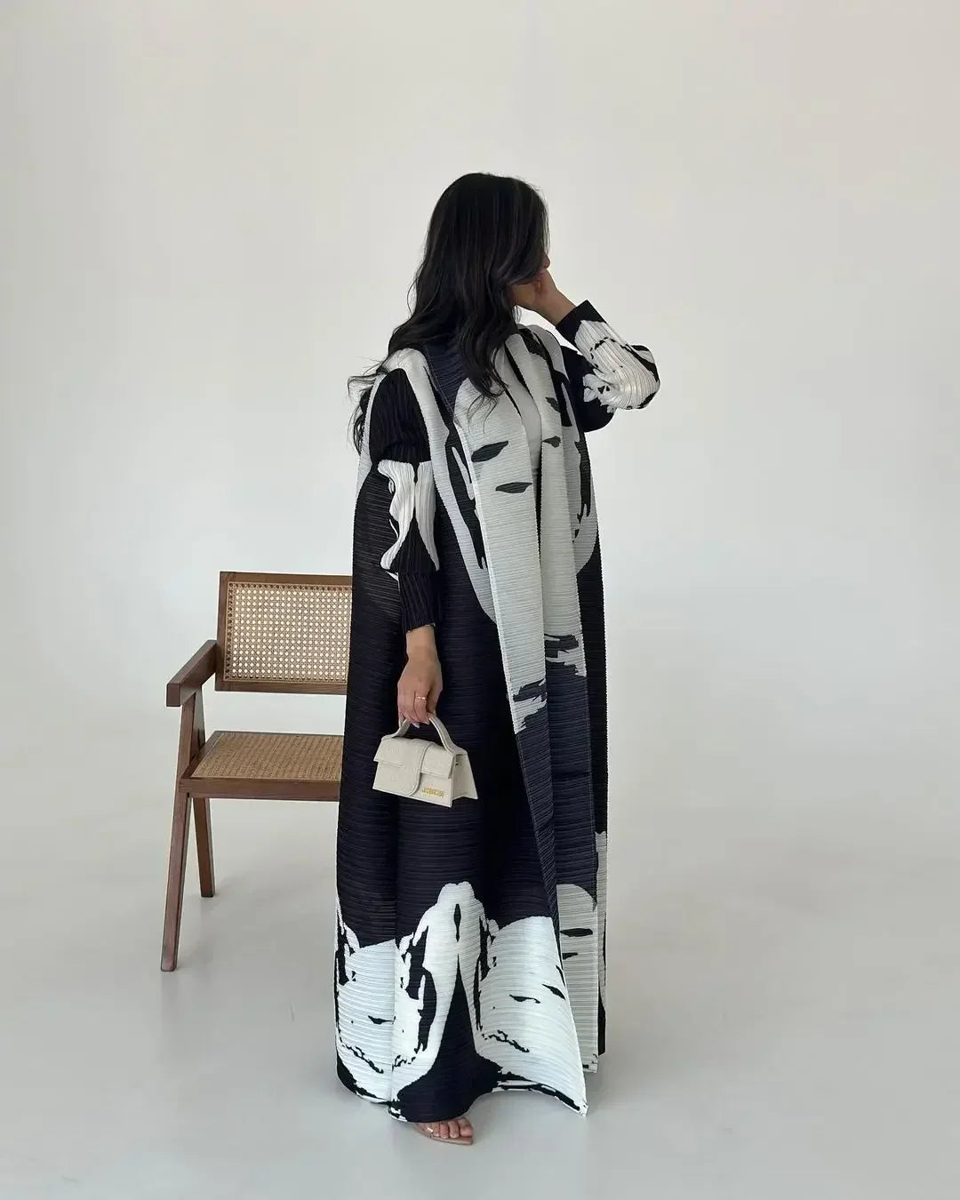Person wearing a black and white patterned outfit with a long coat, standing against a plain background.