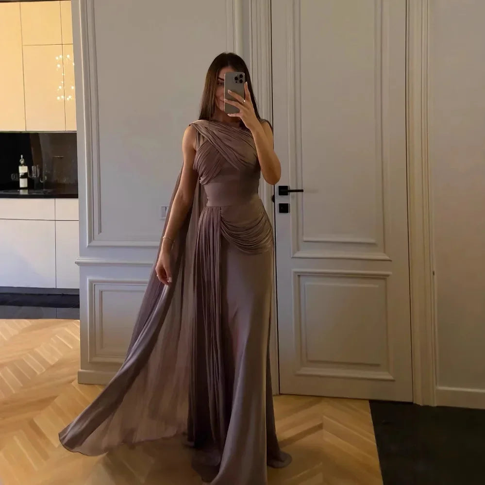 Woman taking a mirror selfie wearing a long, flowing dress in a room with white walls and wooden floor.