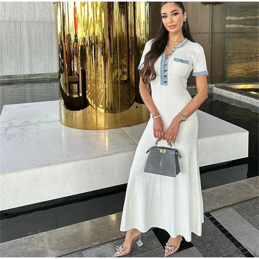 Woman in a white dress holding a gray handbag in an indoor setting with decorative elements.