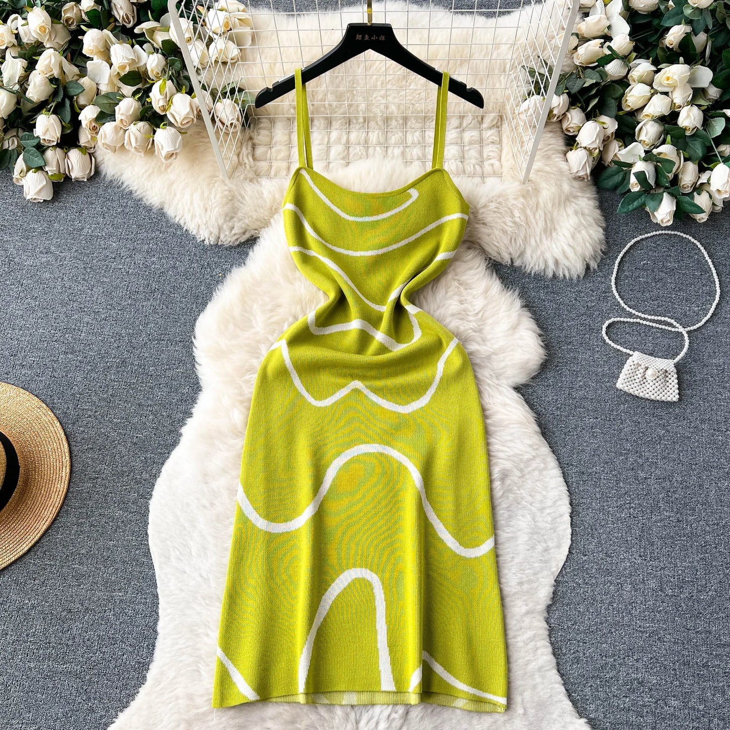 Green dress with white patterns on a hanger against a textured surface with decorative elements.