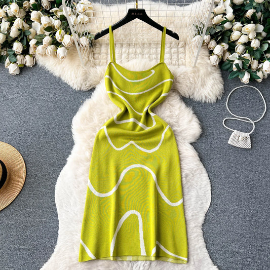 Green dress with white patterns on a hanger against a textured surface with decorative elements.