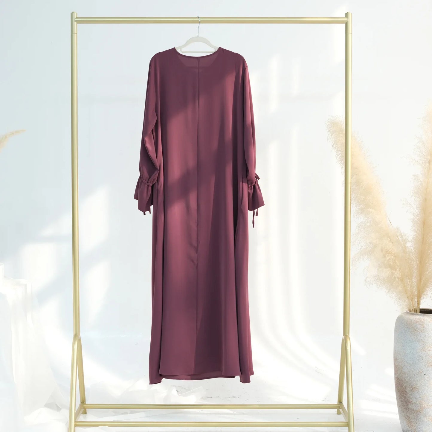 Maroon dress hanging on a gold rack against a white background
