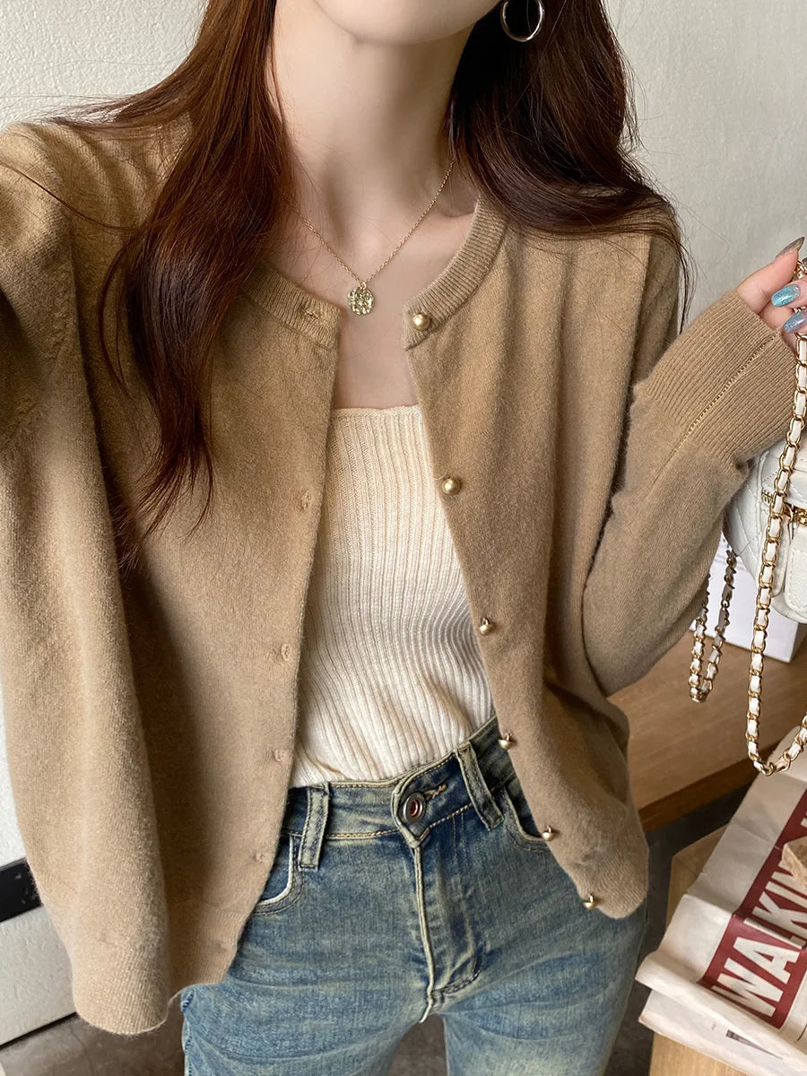 Person wearing a beige cardigan over a white top and blue jeans, holding a handbag.