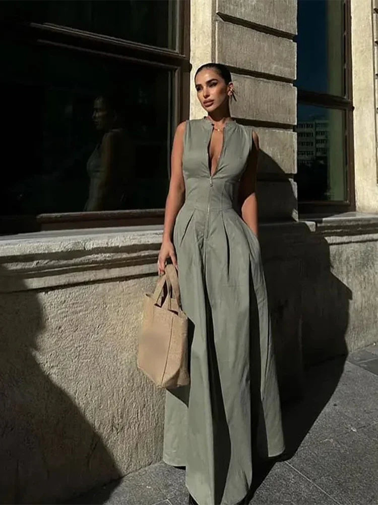 Woman in a long green dress standing against a building wall.