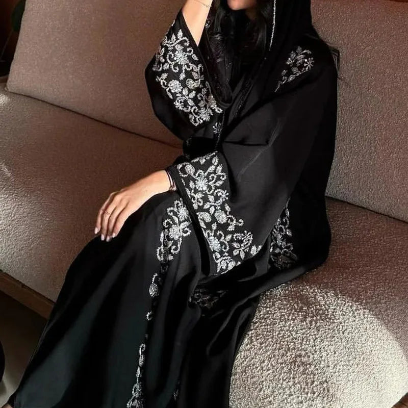 Person wearing a black abaya with white embroidery sitting on a brown couch.