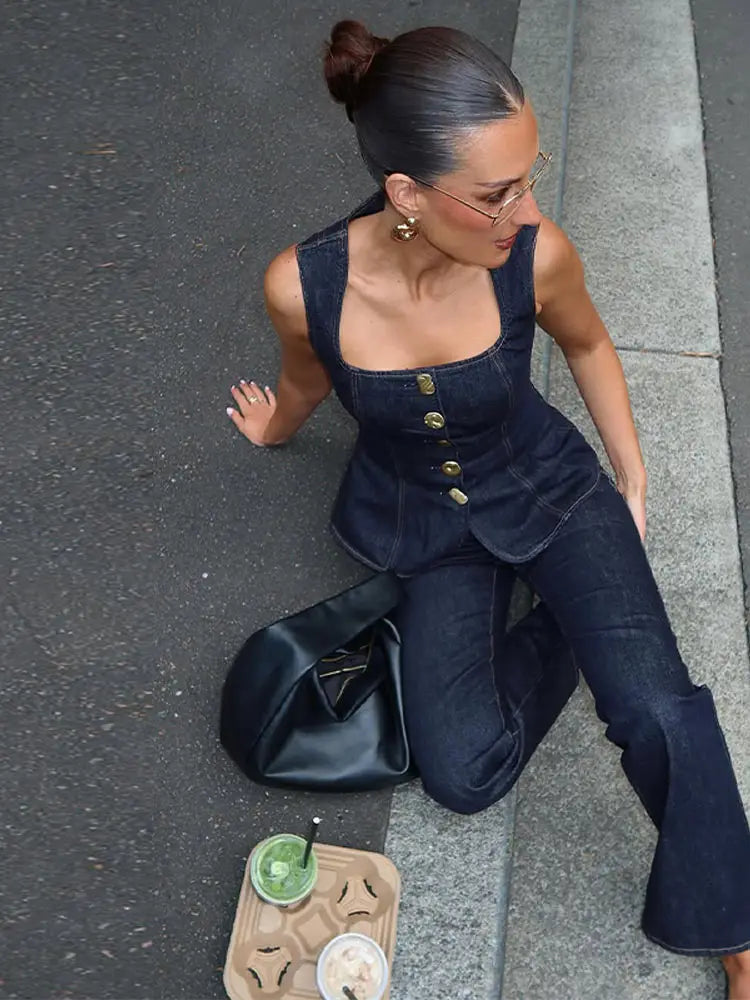 Woman sitting on a sidewalk with a black bag and a drink container next to her.