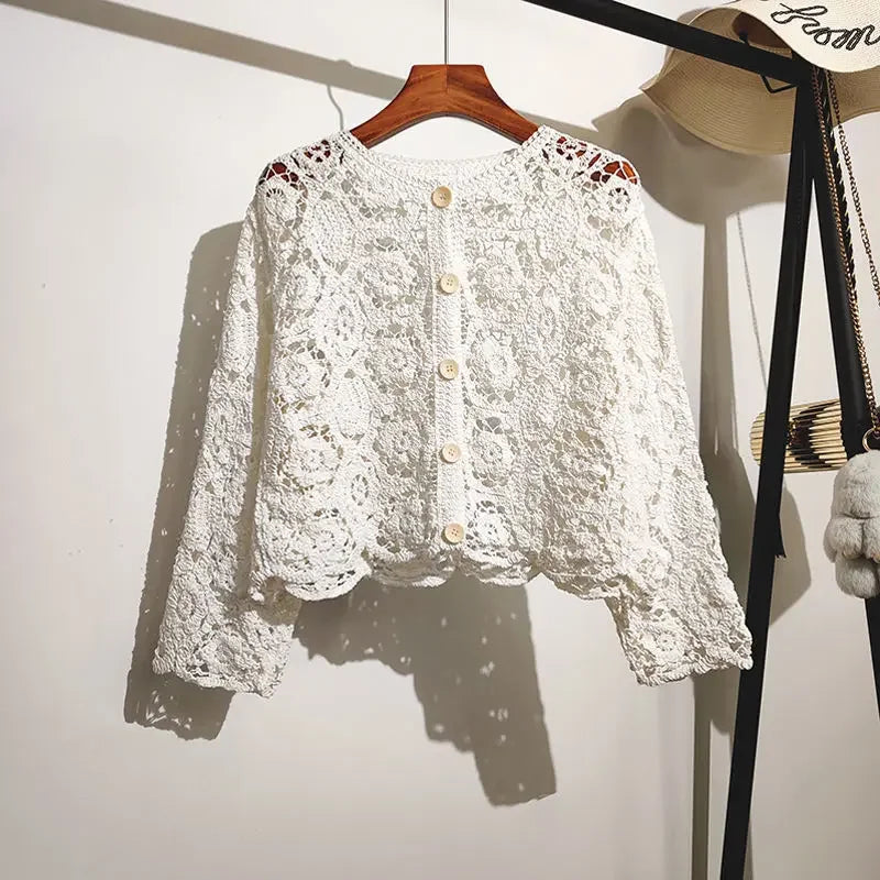 White lace cardigan on a wooden hanger against a white wall.