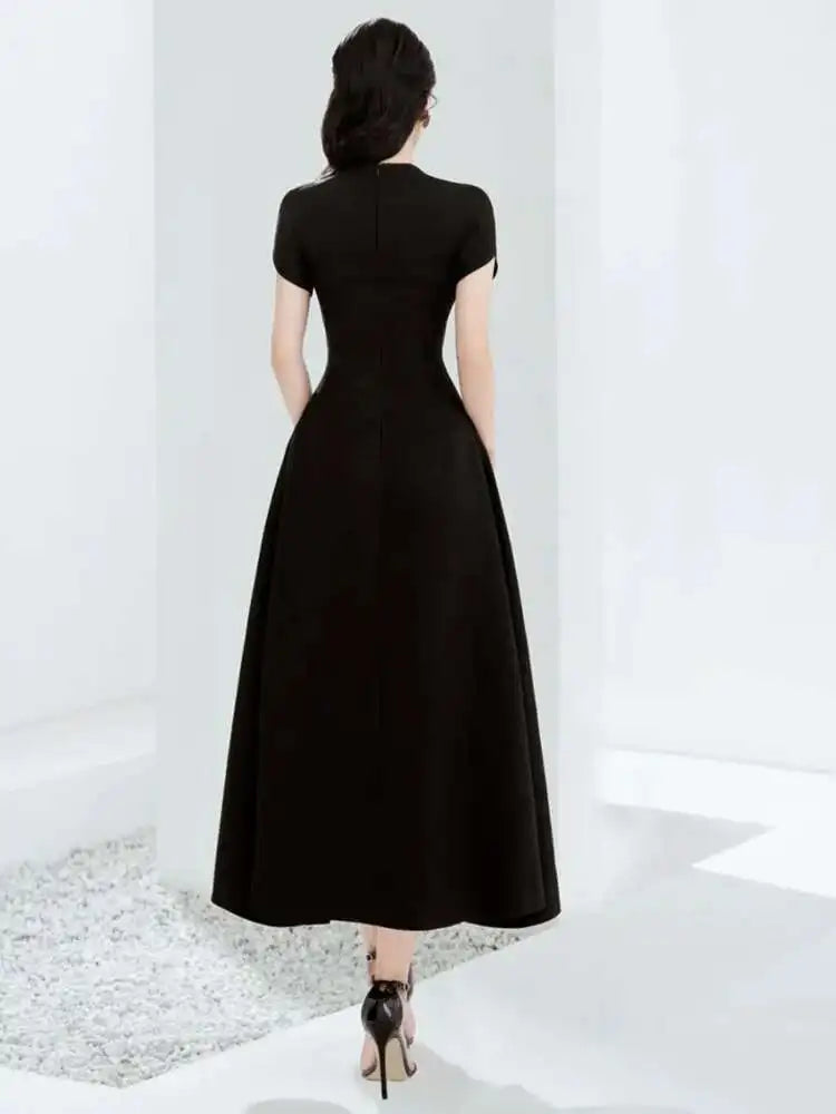 Woman wearing a black dress standing in a minimalistic room with white walls and floor.
