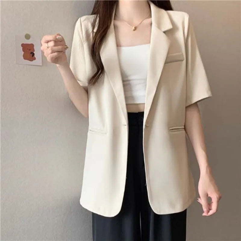 Person wearing a beige blazer over a white top and black pants on a plain background