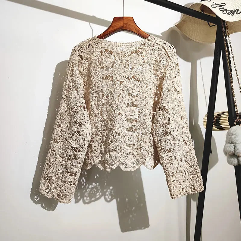 Beige lace sweater on a wooden hanger against a white wall.