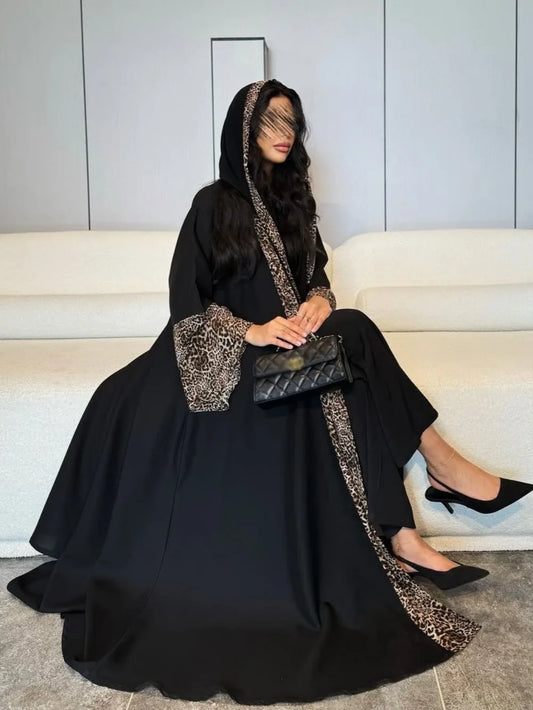 Woman in a black abaya with leopard print trim sitting on a white couch.