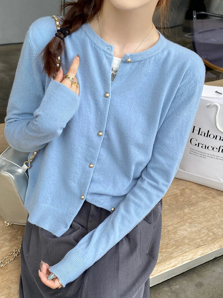 Person wearing a light blue cardigan with gold buttons in an indoor setting.