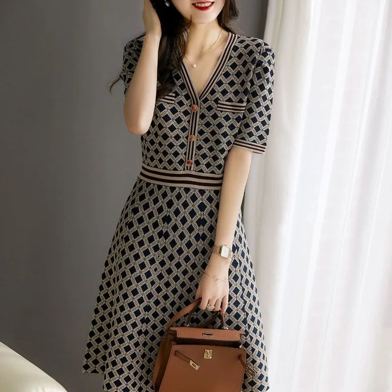 Woman wearing a patterned dress holding a brown handbag indoors.