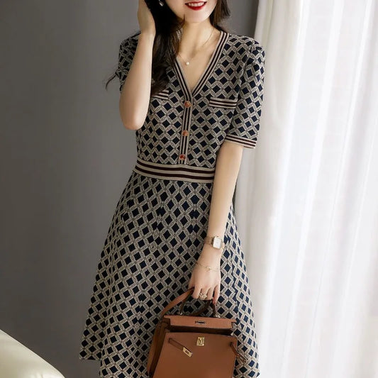 Woman wearing a patterned dress holding a brown handbag indoors.