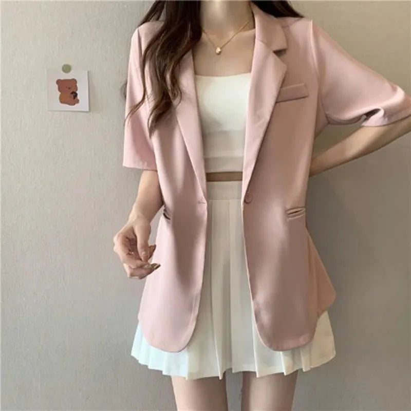 Person wearing a pink blazer over a white top and skirt against a plain background