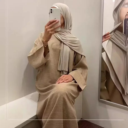 Person wearing a beige outfit and hijab taking a mirror selfie.