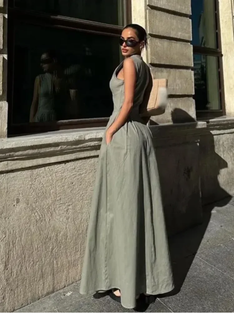 Woman in a long green dress standing against a building wall.