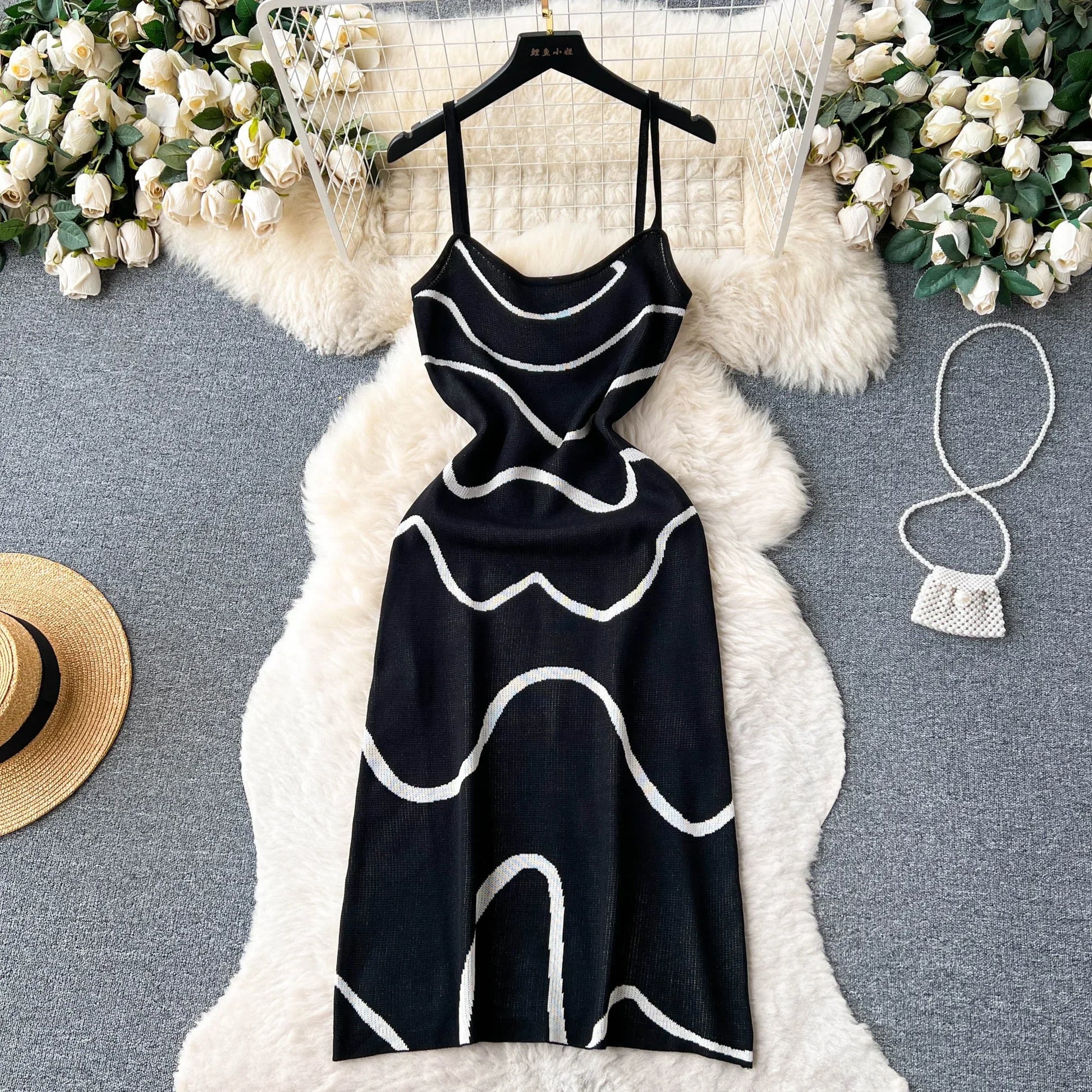 Black dress with white patterns on a hanger against a floral and textured background