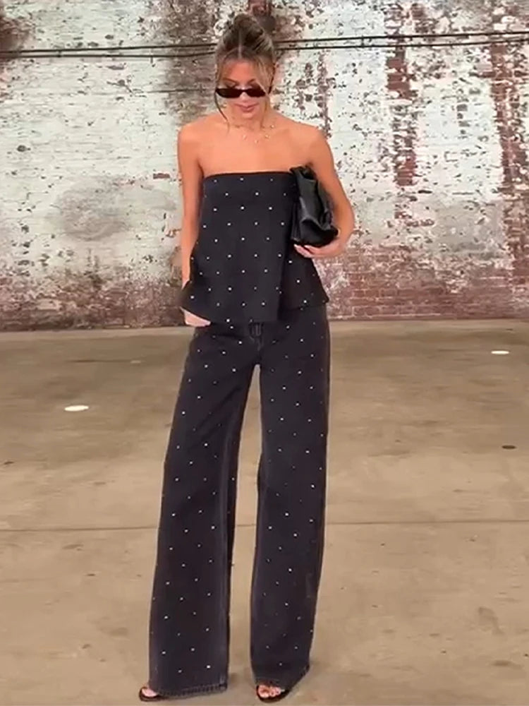 Woman wearing a black strapless top and wide-leg pants with a textured wall background