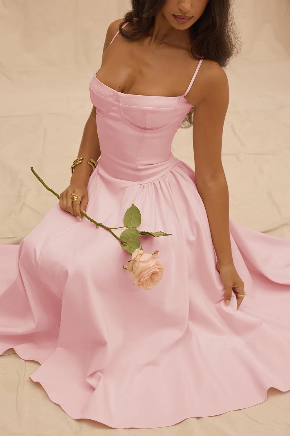 Woman in a pink dress holding a rose against a beige background