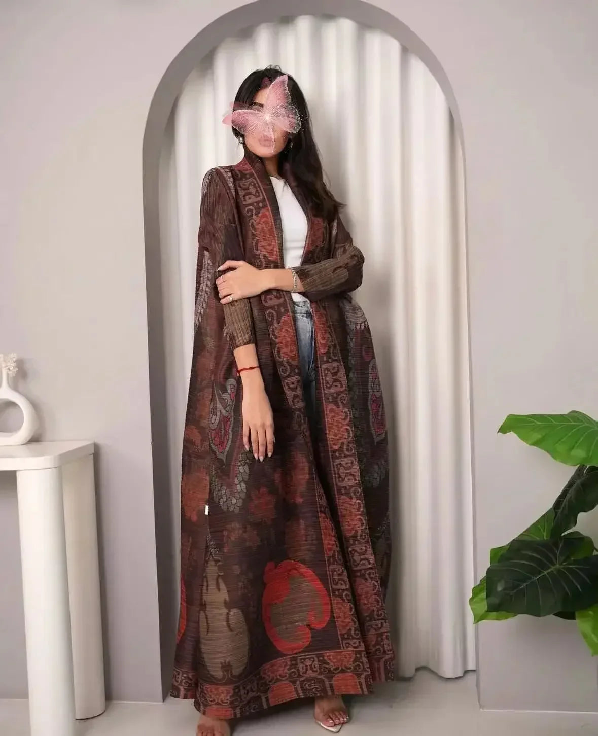 Woman wearing a long, patterned dress standing in a room with a white archway and plant.