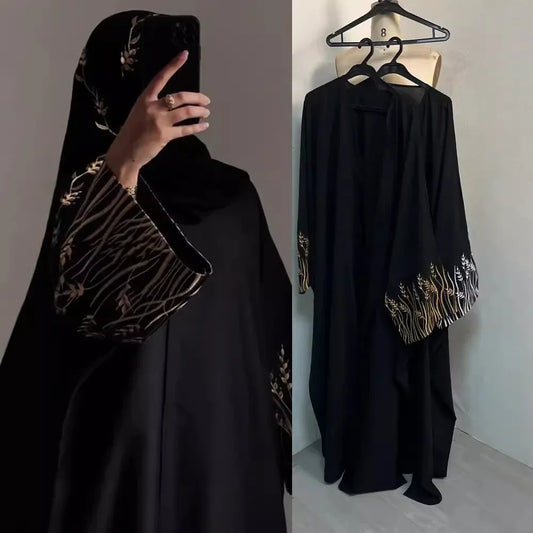 Black abaya with gold embroidery worn by a person and hanging on a mannequin.